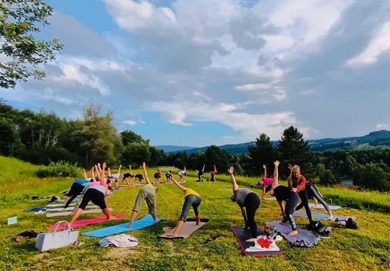 Outdoor Yoga Session on Hillside Meadow Group practicing yoga on mats outdoors on a green hillside under a cloudy sky.