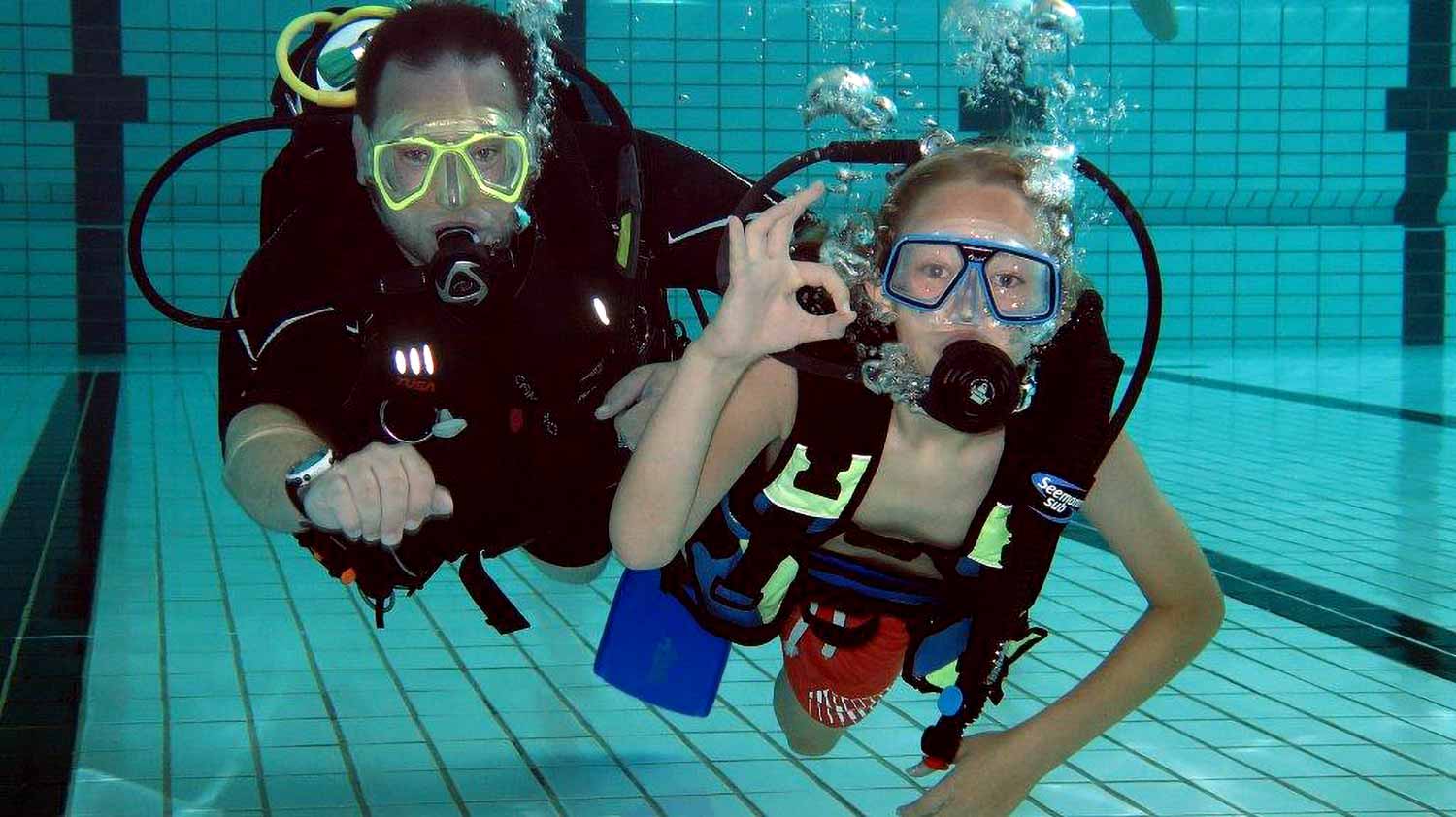 Divers Underwater in Pool Scuba instructor and young diver giving an okay sign underwater in a pool.