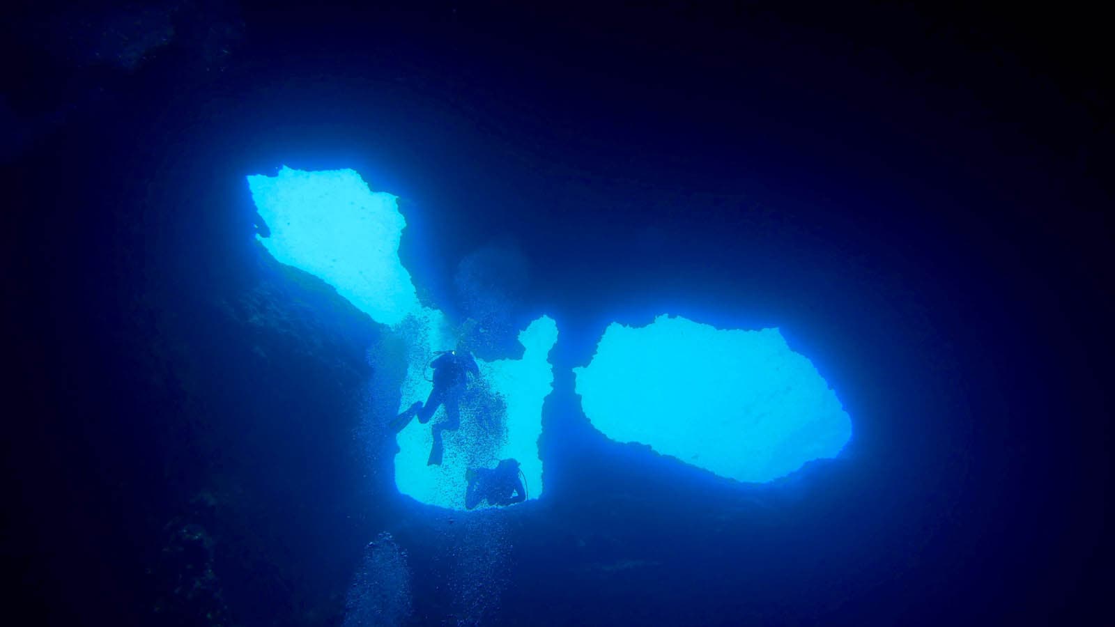 Diver in a glowing underwater cave Silhouette of a diver exploring an underwater cave with bright blue light openings.