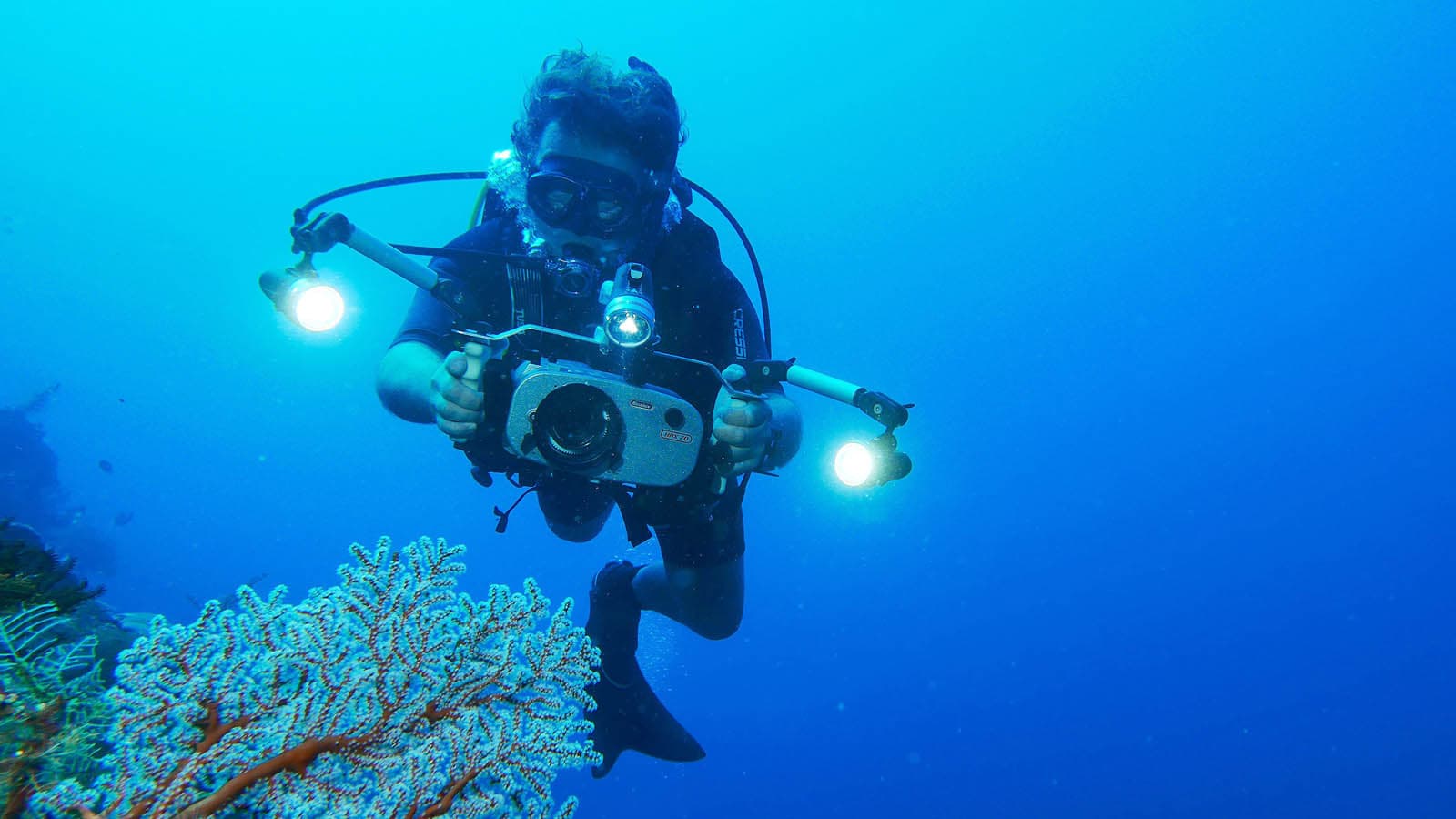 Diver photographs coral reef underwater A diver holds an underwater camera rig with two lights near a coral reef.