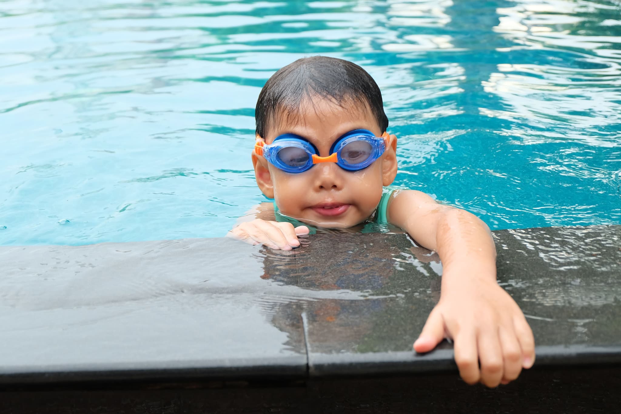 Child Swimming in Pool With Goggles Child wearing blue goggles at the edge of a swimming pool.