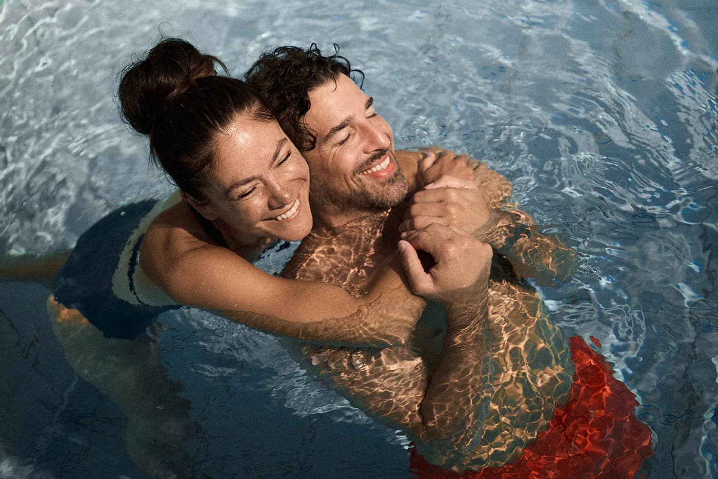 Couple Embracing in Swimming Pool Two people embracing and smiling in a swimming pool with clear blue water.