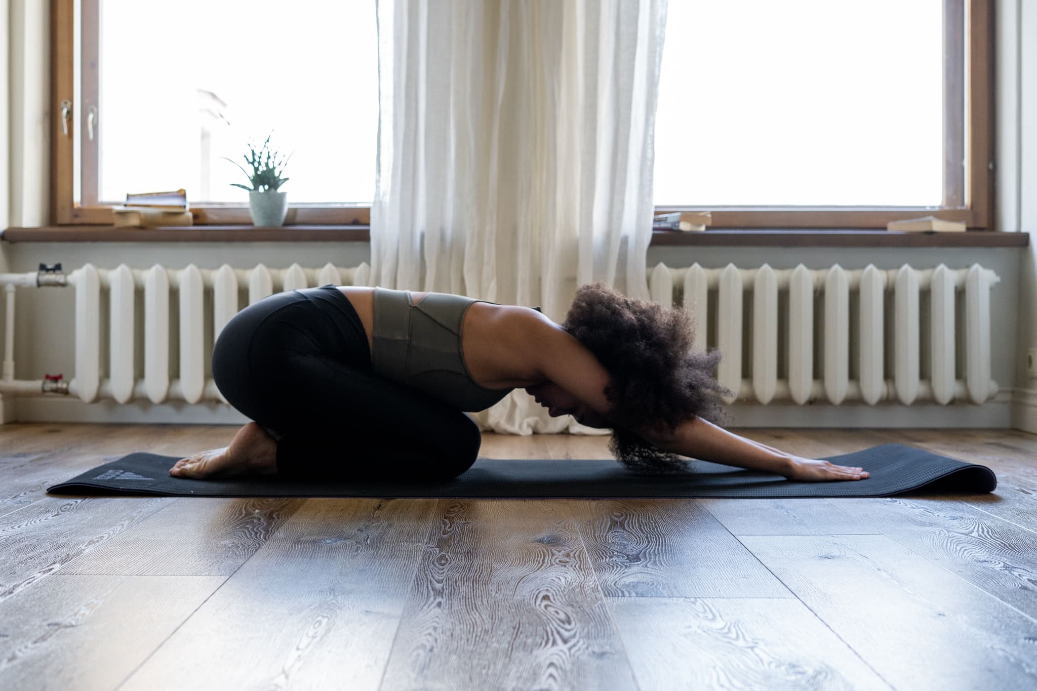 Yoga Practice in Bright Indoor Space Person in a yoga pose on a mat in a bright room with large windows and a radiator.