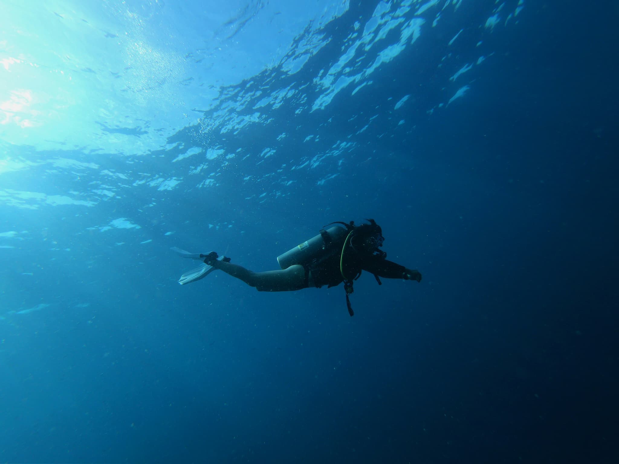 Scuba Diver in Blue Ocean Water Scuba diver in full gear swimming underwater in clear blue ocean water with sunlight filtering from above.