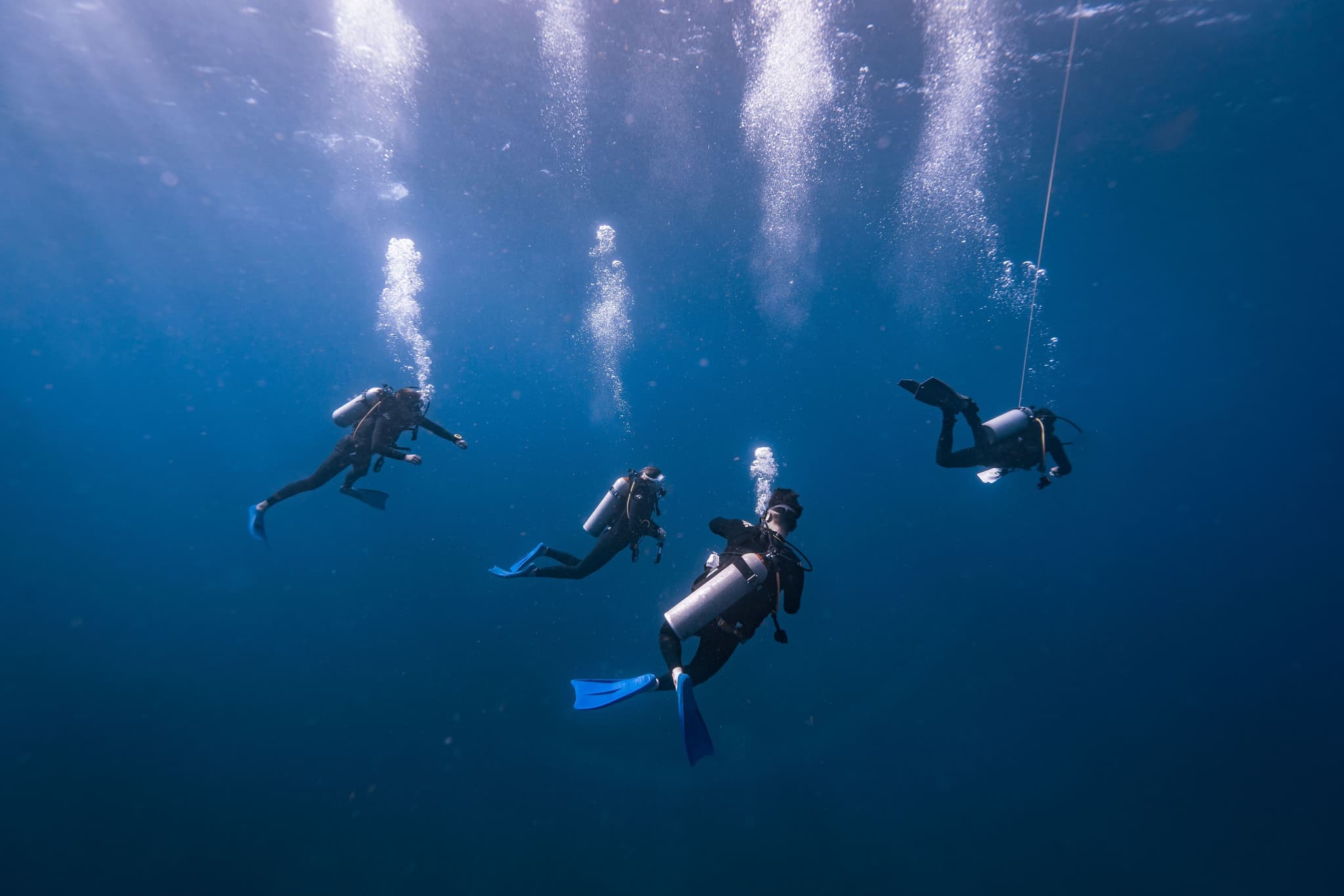 Scuba Divers in Clear Blue Water Four scuba divers underwater in clear blue water with air bubbles rising toward the surface.