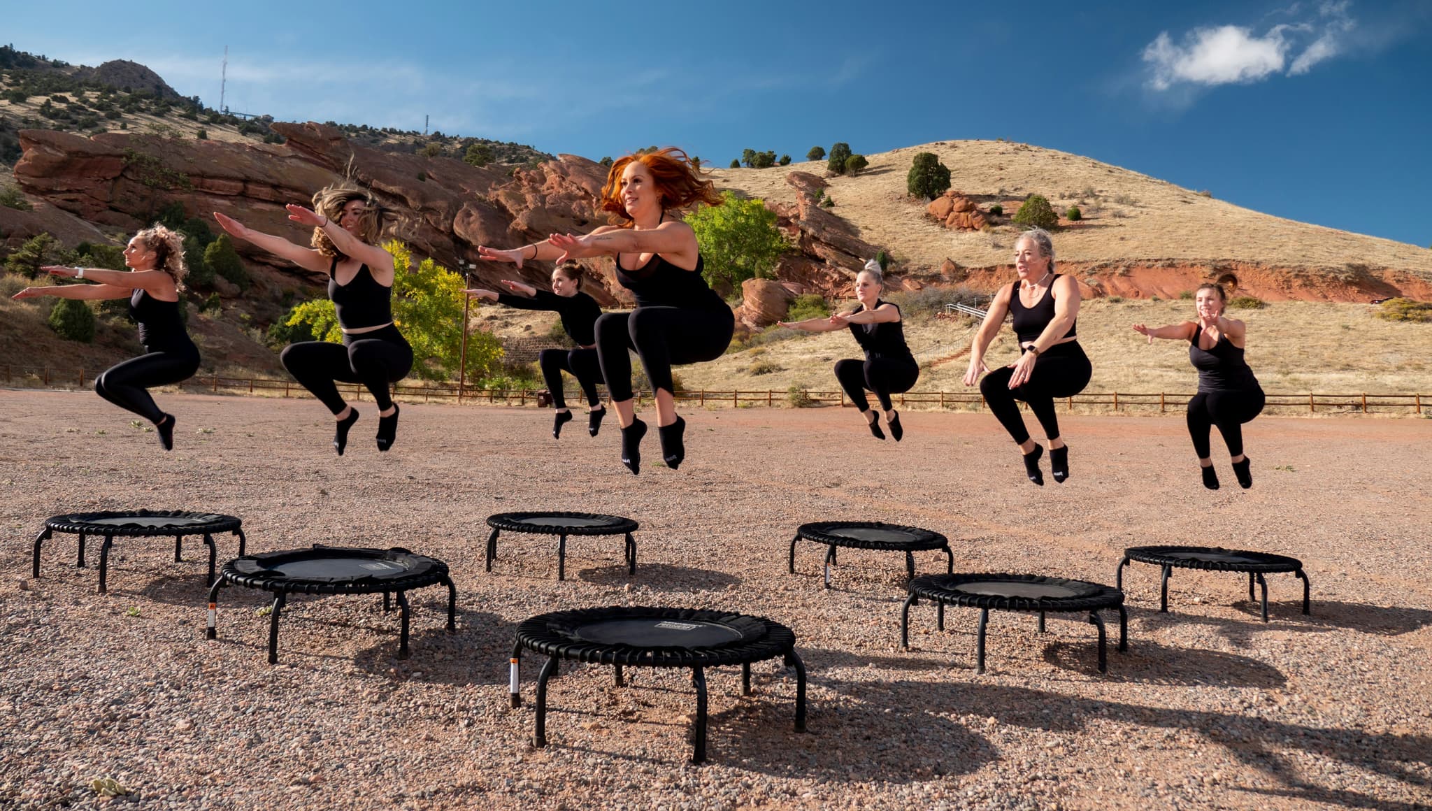 Outdoor Trampoline Fitness Class Group of people performing synchronized trampoline exercises outdoors on red earth with red rock hills in the background.