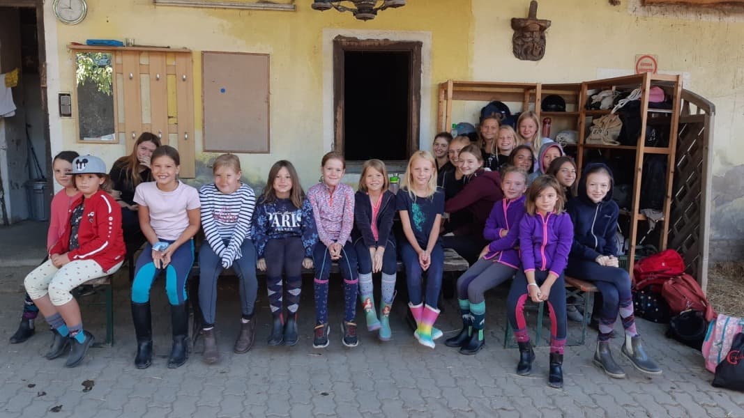 Girls Gathered Outside Rustic Building Group of girls sitting on benches outside a rustic yellow building.