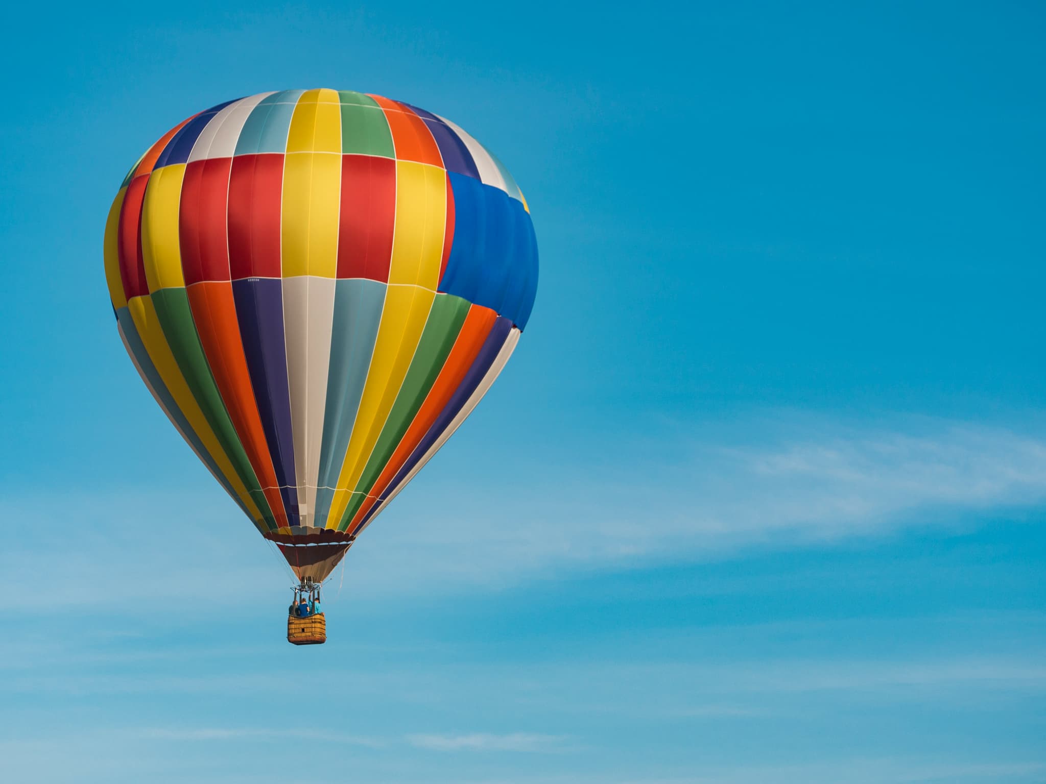 Colorful Hot Air Balloon in Flight A colorful hot air balloon with red, yellow, blue, and green panels floats against a clear blue sky.