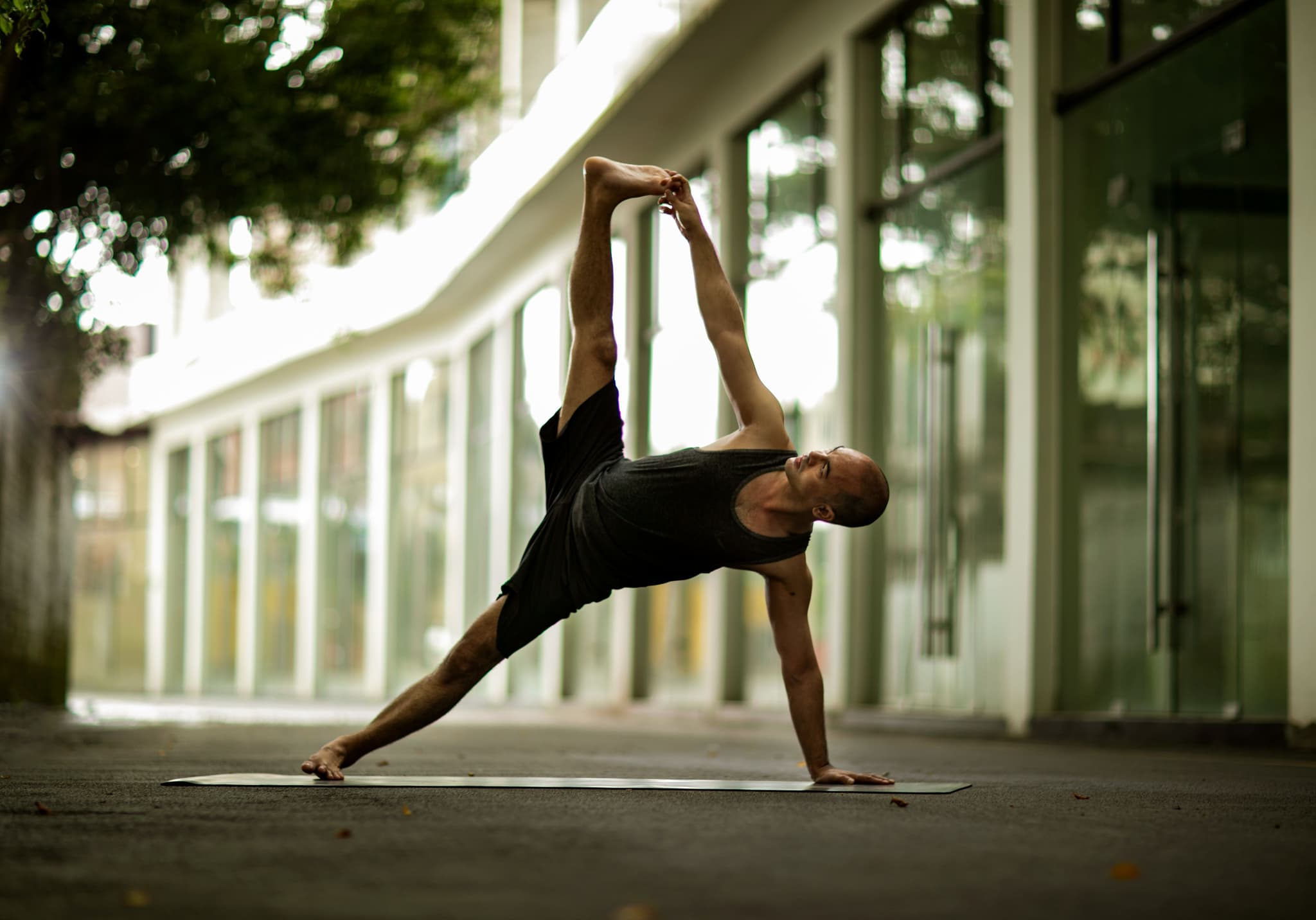 Side Plank Yoga Pose on City Street Man in side plank yoga pose on a mat along an urban street.