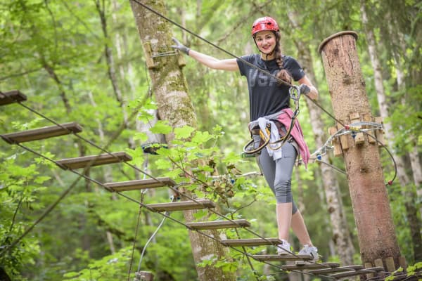 Forest High Ropes Course Adventure Woman in helmet crossing a wooden rope bridge on a forest high ropes course.