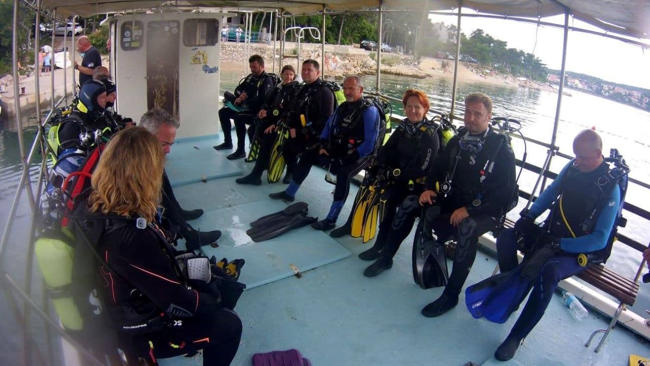Scuba Divers Preparing on Boat Deck Group of scuba divers in wetsuits sitting on a boat deck near the coast.