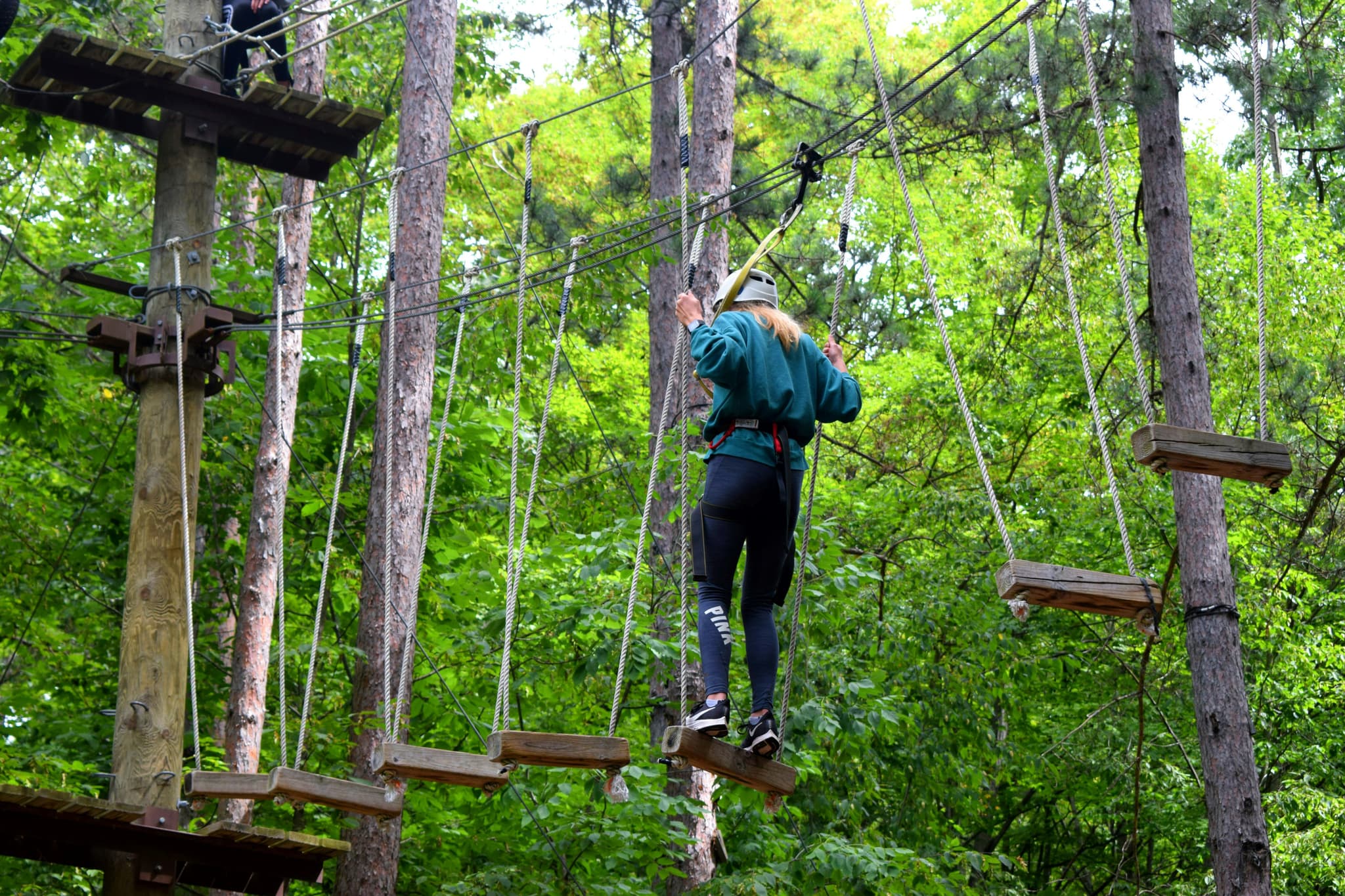 High Ropes Course Crossing Person in helmet crossing a high ropes course between suspended wooden planks.