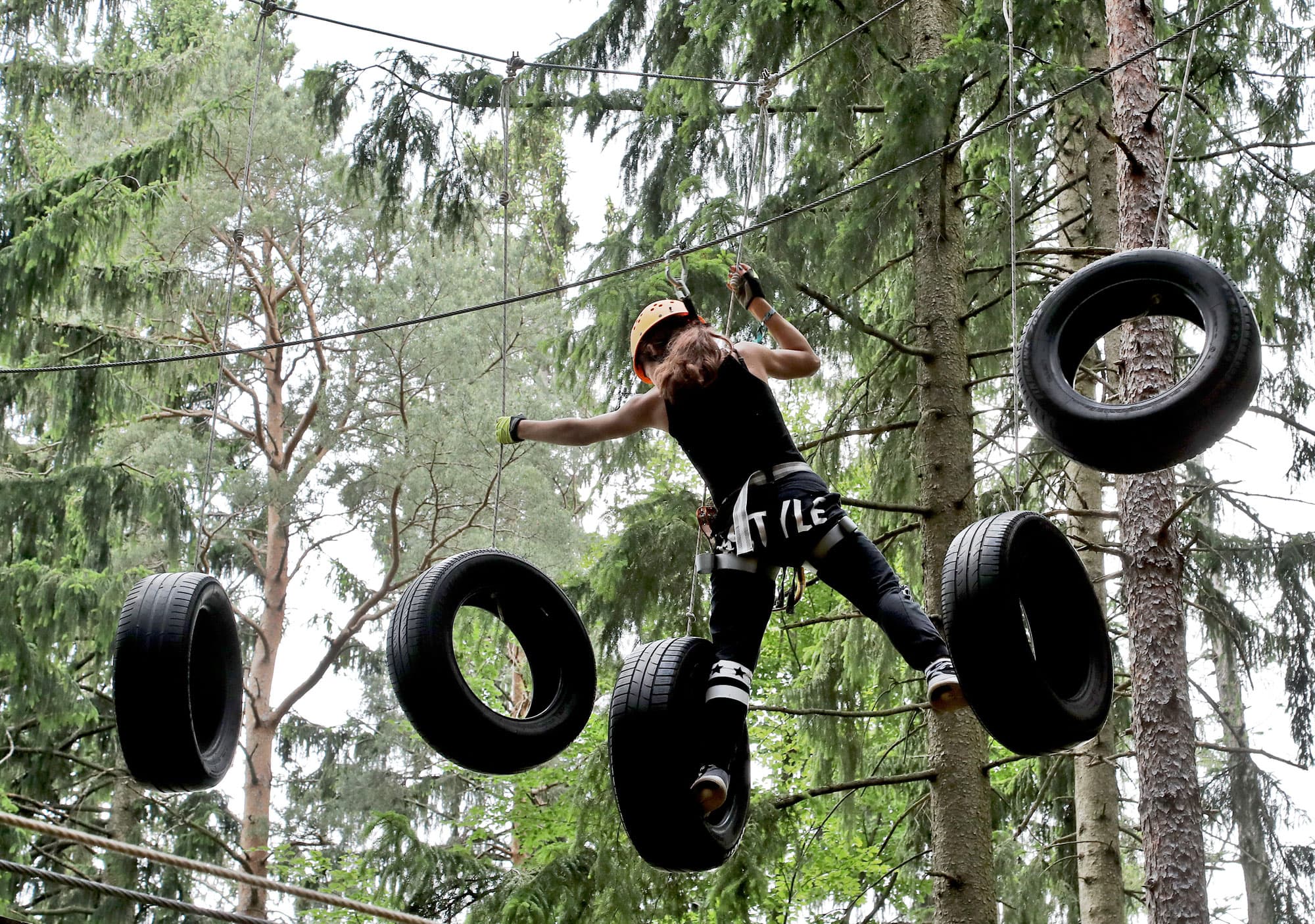 Tire Obstacle Course in the Forest Person in helmet and harness climbing a hanging tire obstacle course among trees.