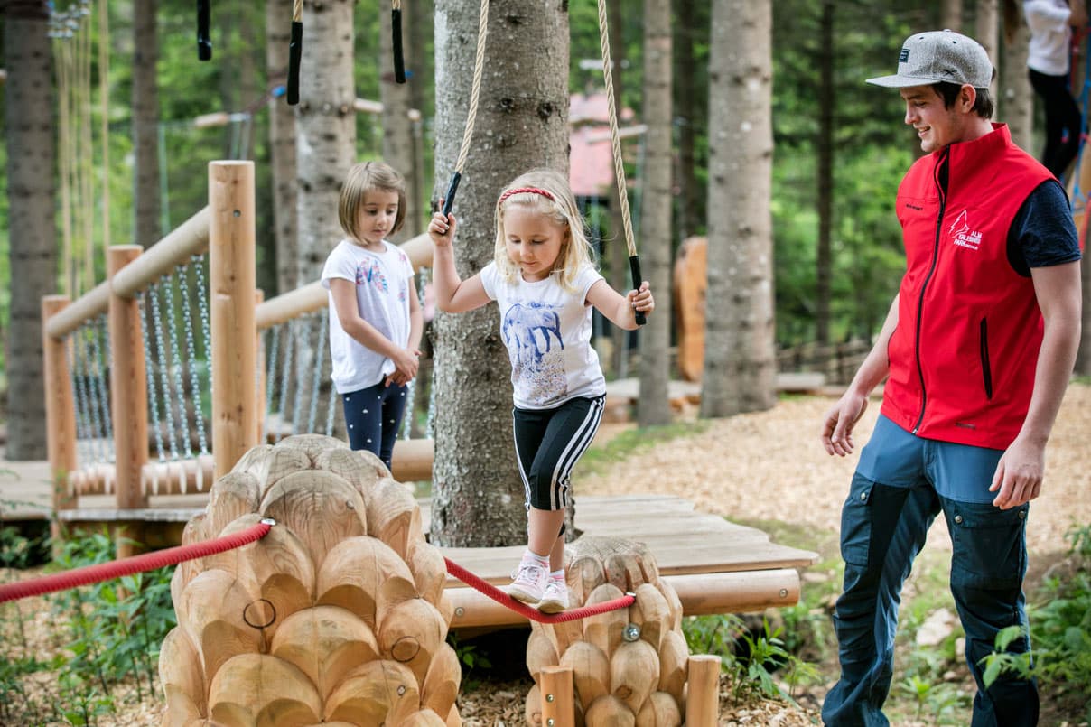 Children on Rope Swings in Forest Adventure Park Two children on rope swings in a forest adventure park with an instructor supervising nearby.