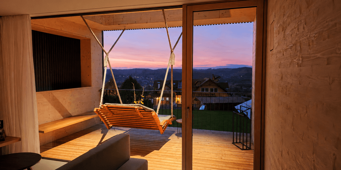 Wooden Deck Swing Mountain Sunset View Modern wooden deck with an orange swing at sunset, overlooking forested mountains and a village valley below.
