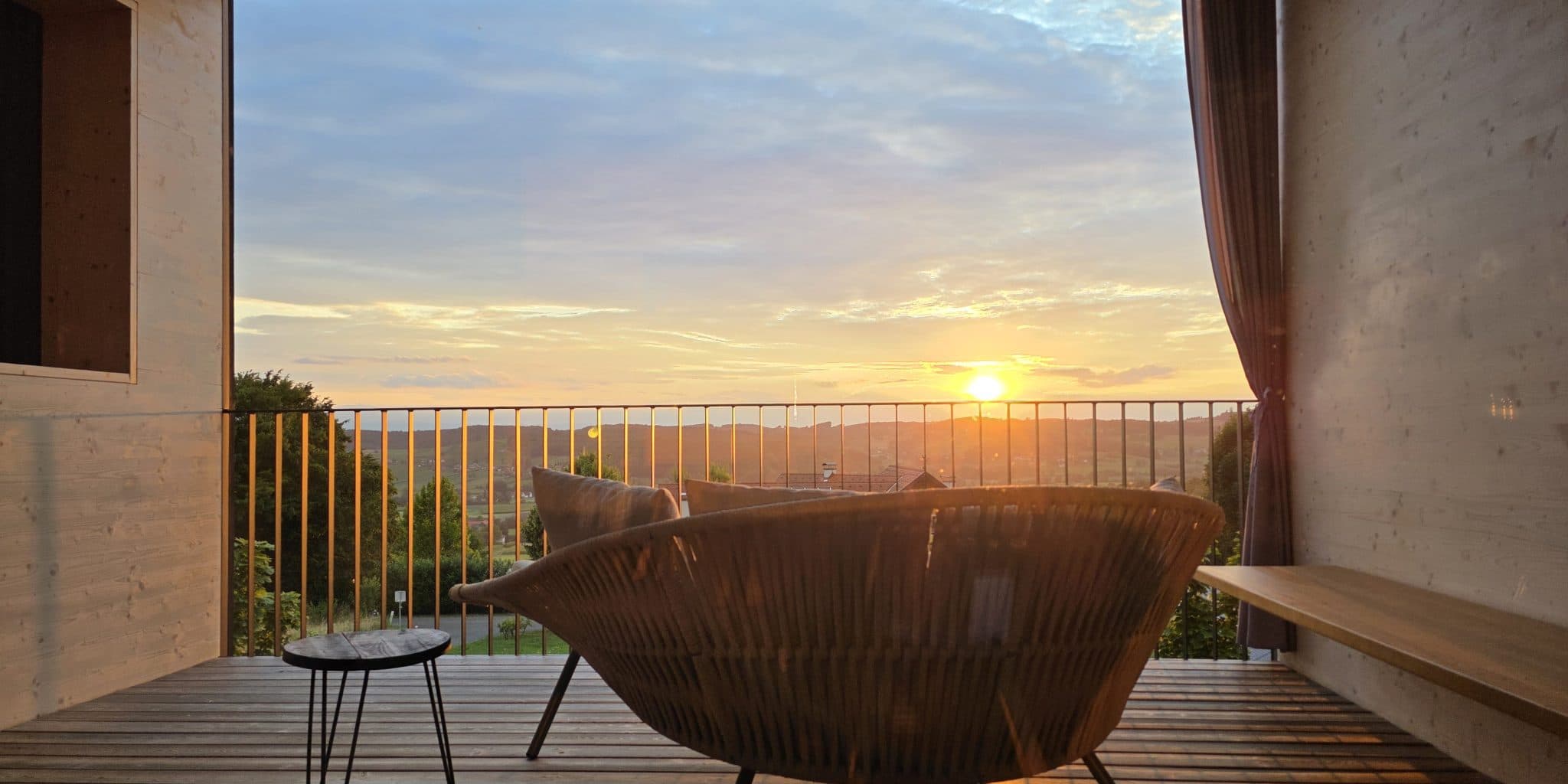 Balkonliege mit Blick auf das Tal bei Sonnenuntergang Moderne Flechtliege auf einer Holzterrasse mit Blick auf ein Tal bei Sonnenuntergang.