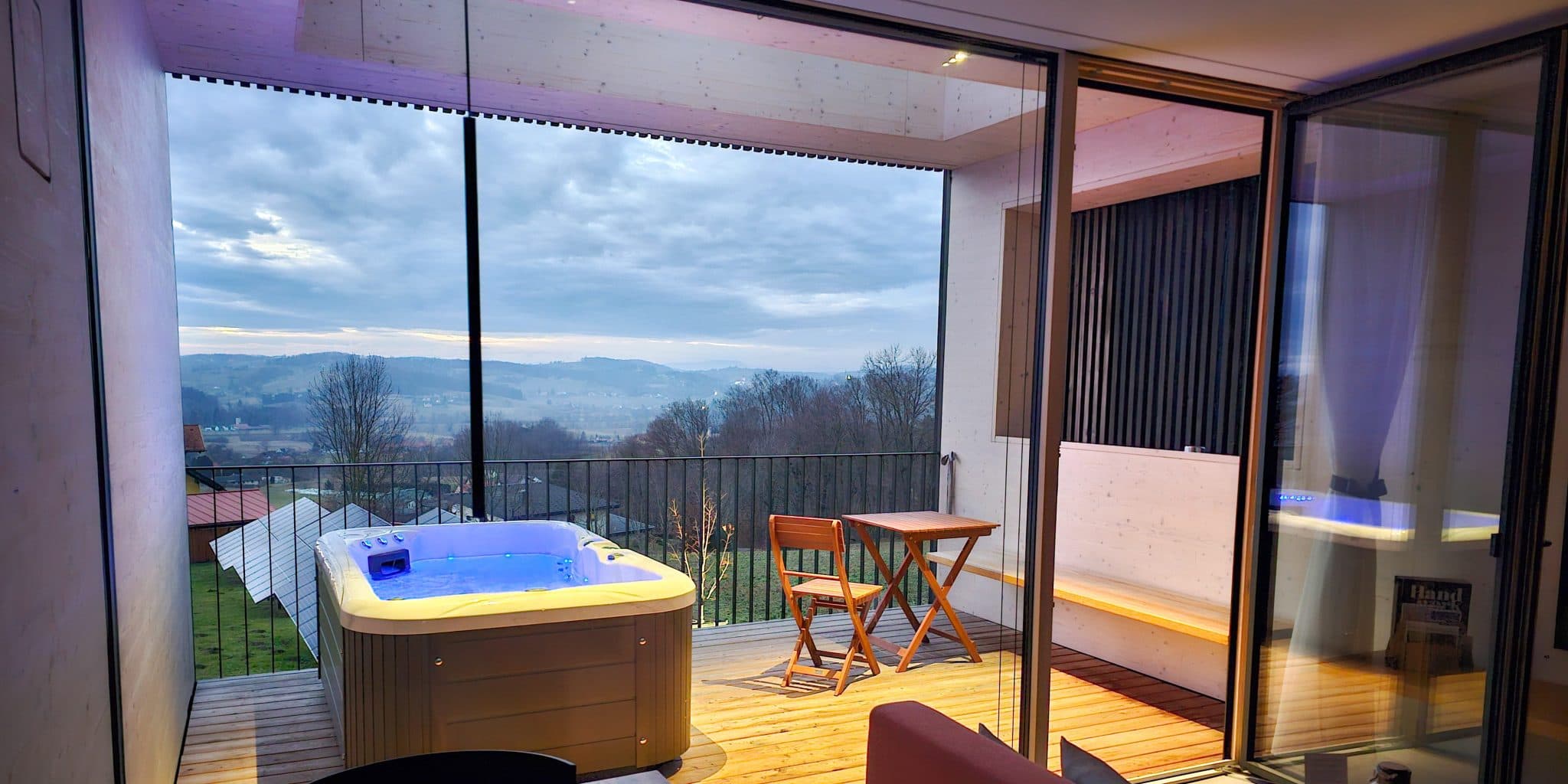 Whirlpool-Terrasse mit Bergtal-Ausblick Whirlpool auf einer Holzterrasse mit Bergtal-Ausblick und modernen Glastüren mit Blick auf sanfte Hügel.