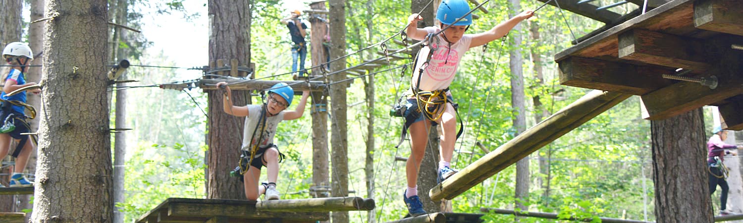 Children Crossing a Rope Bridge in the Forest Children wearing helmets crossing a rope bridge in a high ropes course in the forest.