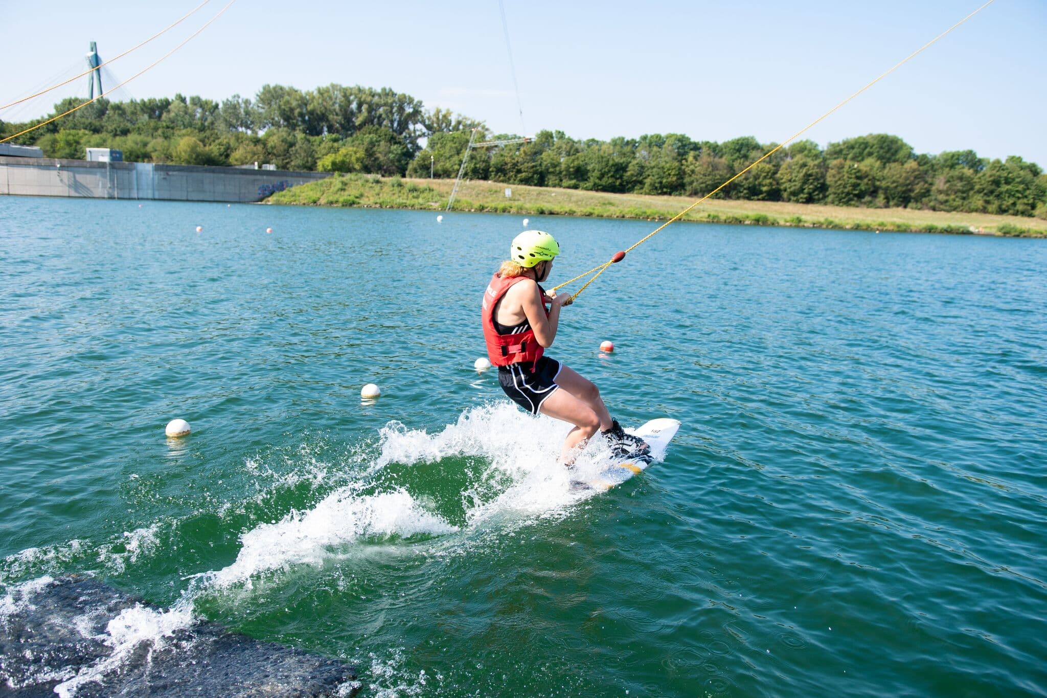 Wakeboarder on the water with tow rope Wakeboarder in red life vest and helmet riding on the water while holding a tow rope, with buoys marking the course and a
