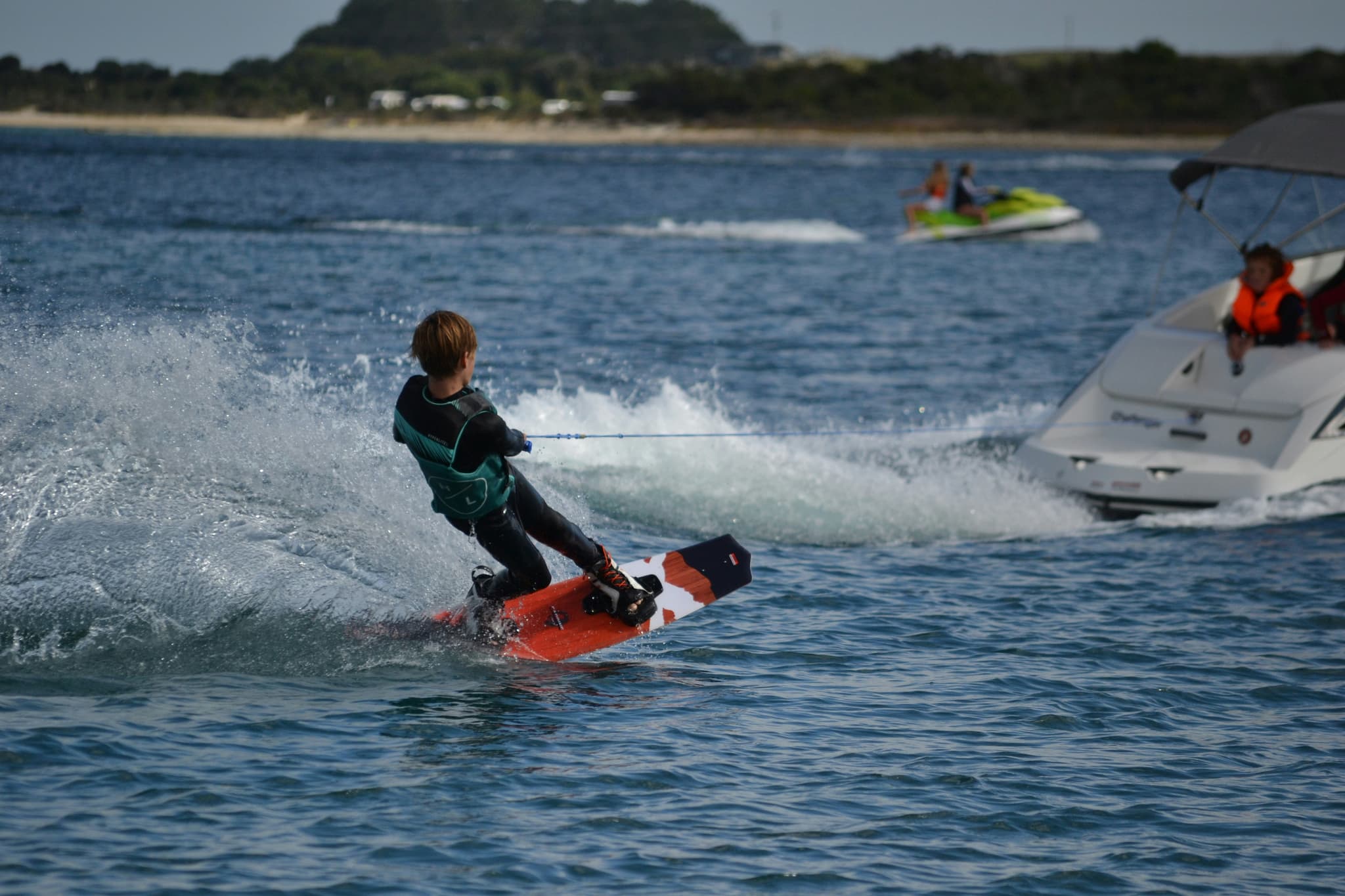 Child wakeboarding behind a boat Child wakeboarding behind a boat on coastal water with waves and a sandy beach in the background.