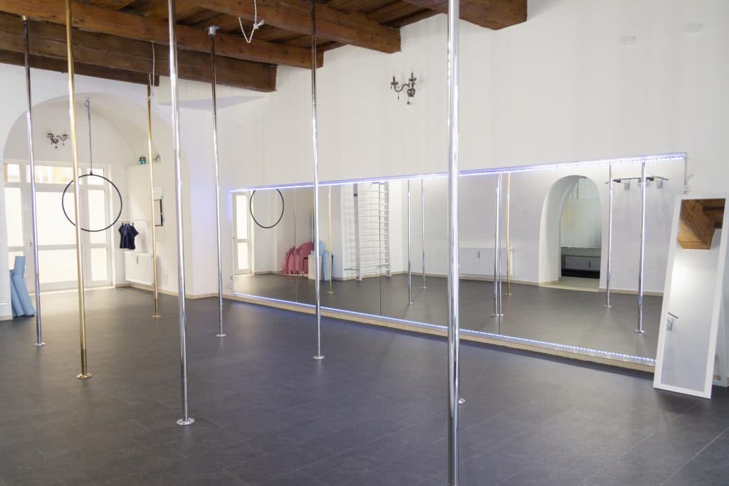 Pole Dance Studio Interior with Mirrors Interior of a pole dance studio with multiple chrome poles, mirrored walls, wooden ceiling beams, and dark flooring.