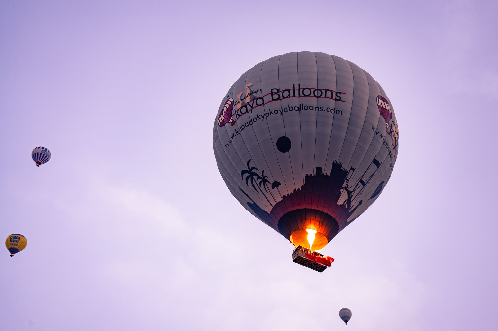 Hot Air Balloons at Dawn Hot air balloons floating in a purple dawn sky, with the main balloon's burner flame glowing orange.