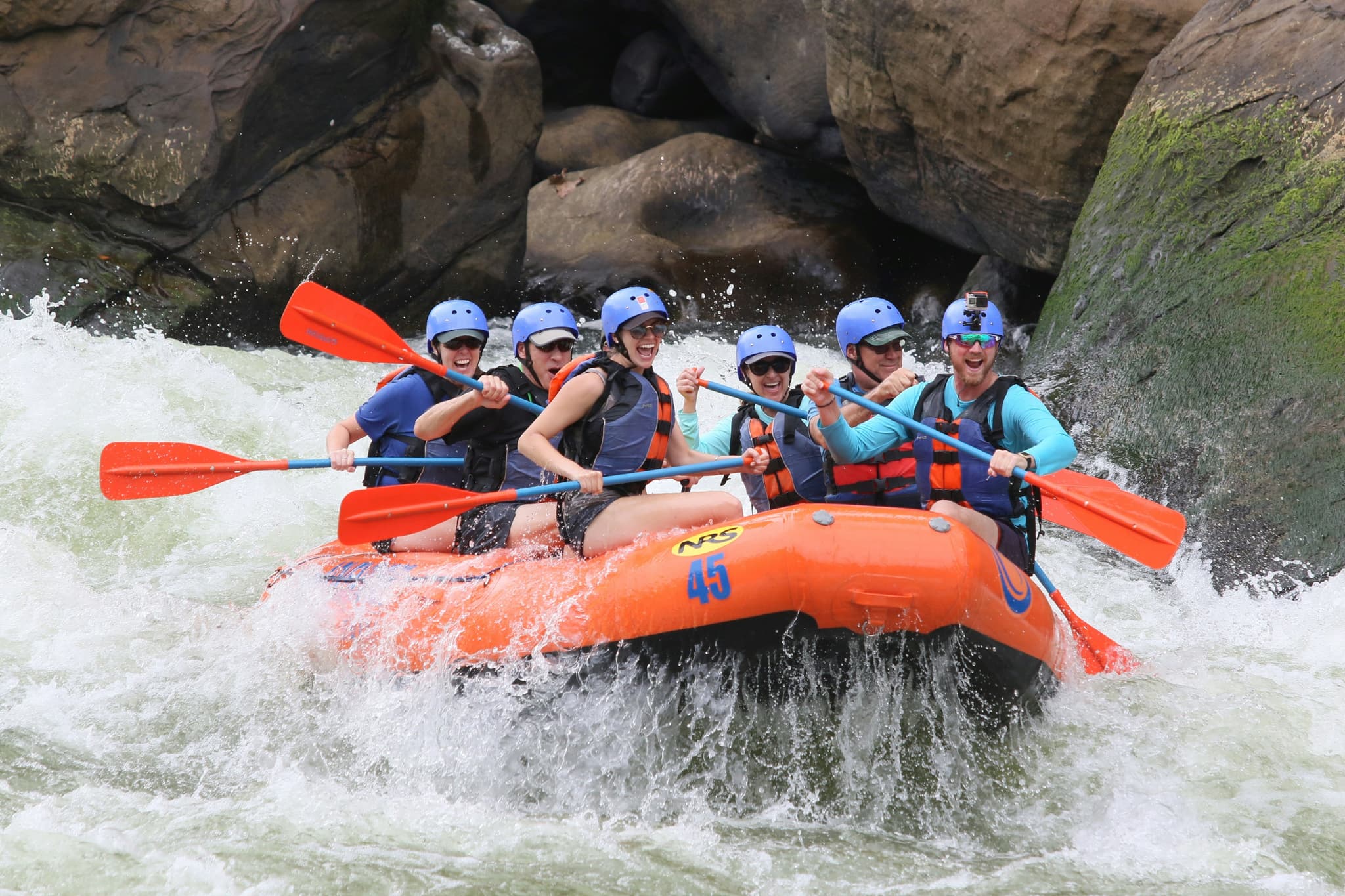 Whitewater Rafting Group in Rocky Canyon Six people paddling an orange raft through whitewater rapids between rocky canyon walls.