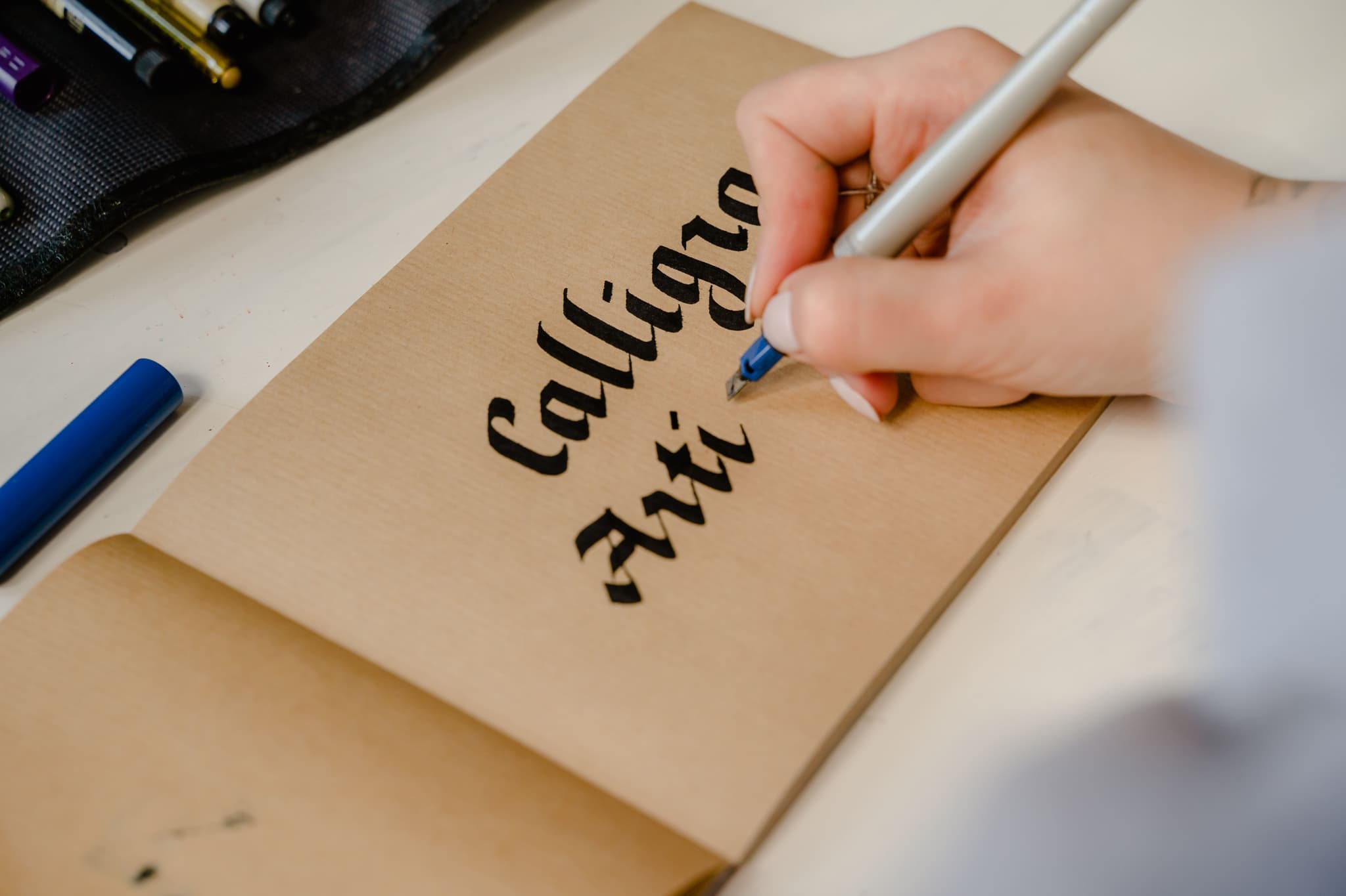 Hand Writing on Kraft Paper Hand writing the words 'calling now' on kraft paper with a blue pen.
