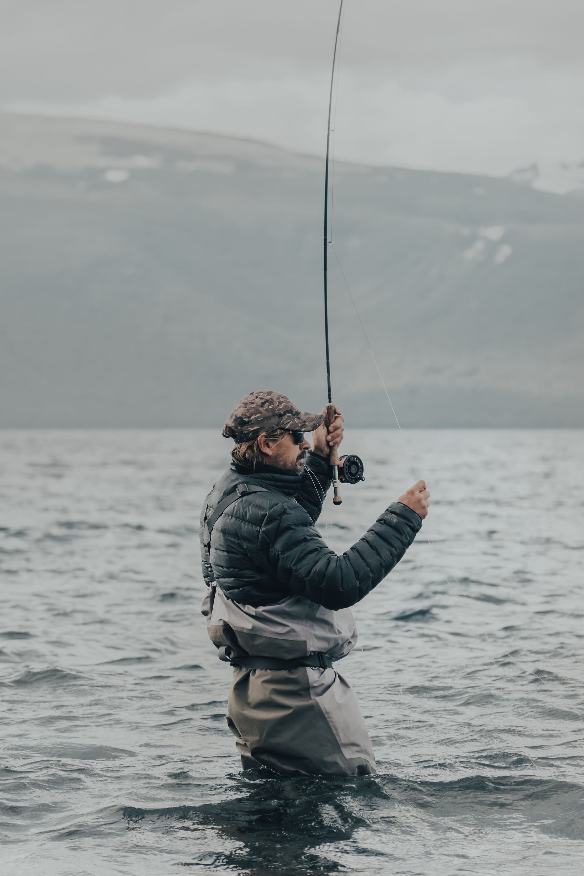 Fly Fishing in Mountain Lake Person fly fishing in a lake with mountains visible in the misty background.