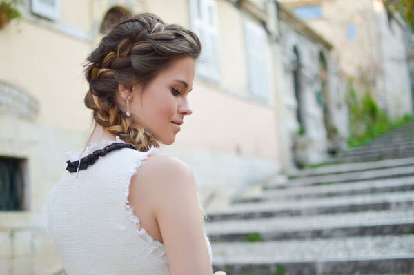 Woman with braided hairstyle on stone steps Woman with braided hairstyle in white dress, standing on stone steps with historic building in the background.