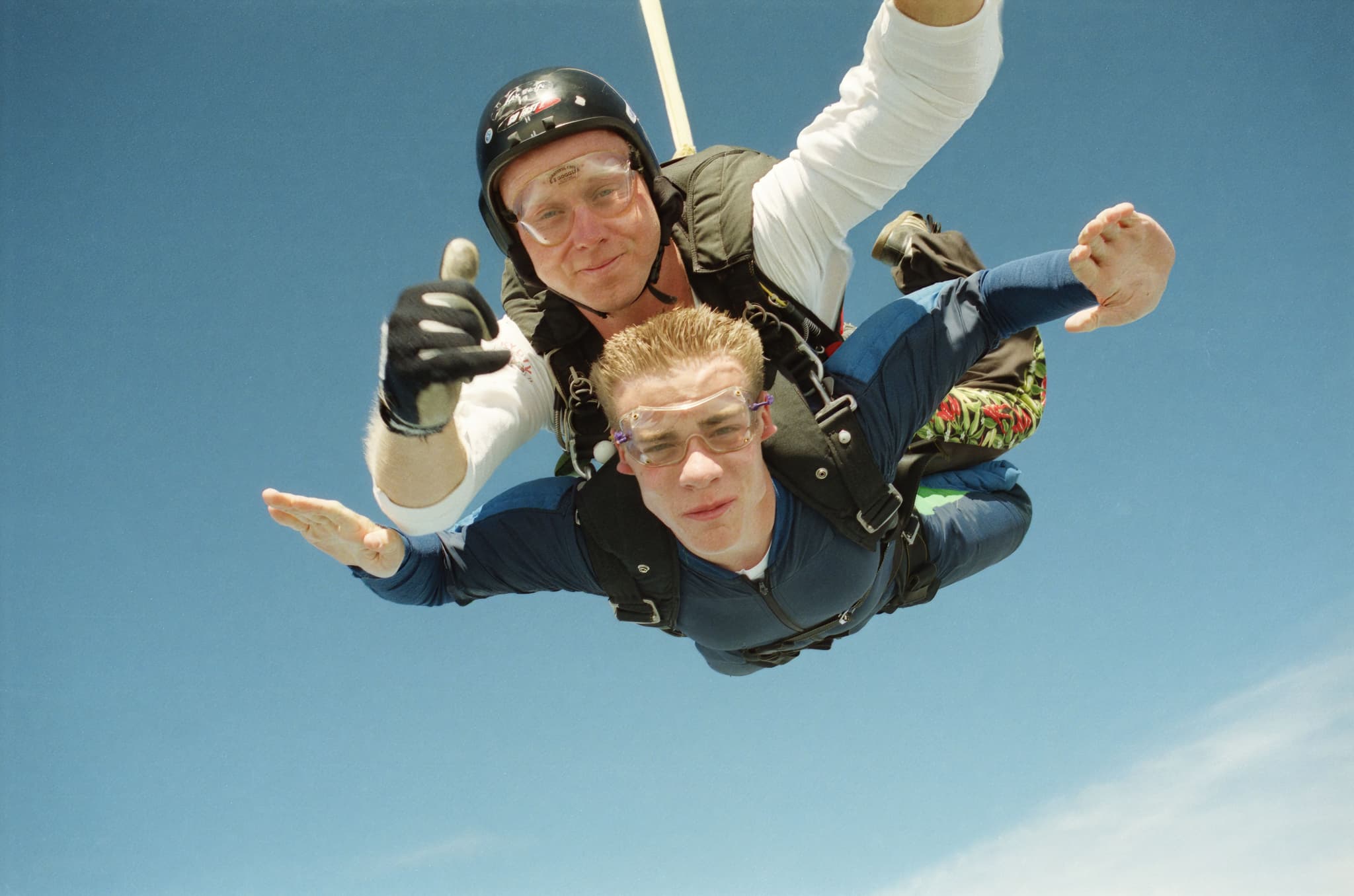 Tandem Skydiving Freefall Tandem skydiving instructor and student in freefall against a clear blue sky.