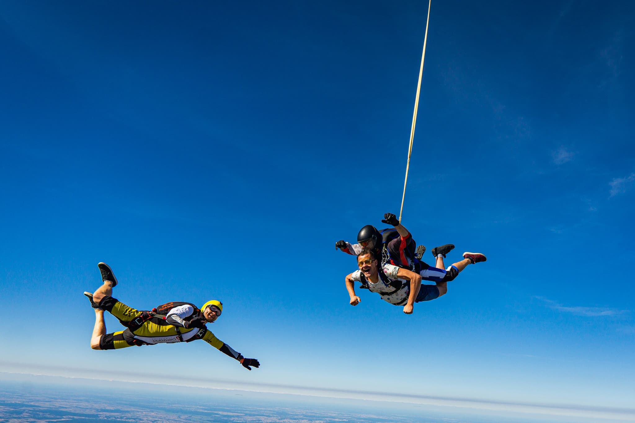 Skydivers in Freefall Formation Three skydivers in freefall formation against a clear blue sky with landscape visible below.
