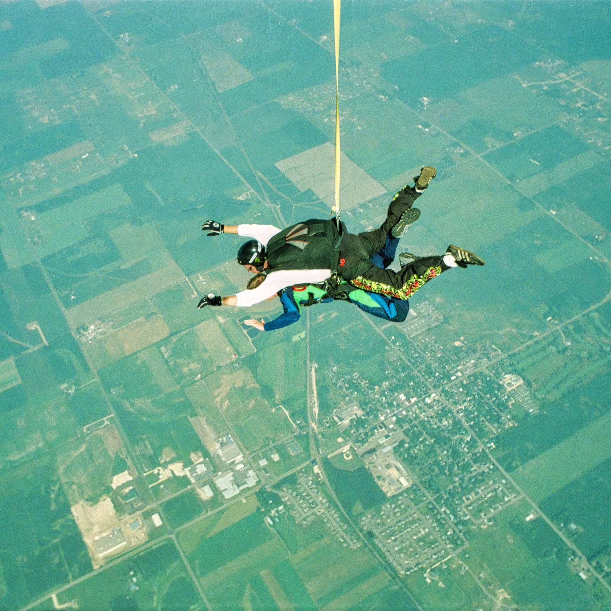 Tandem Skydiving Over Farmland Two skydivers in tandem freefall above patchwork farmland and rural landscape.