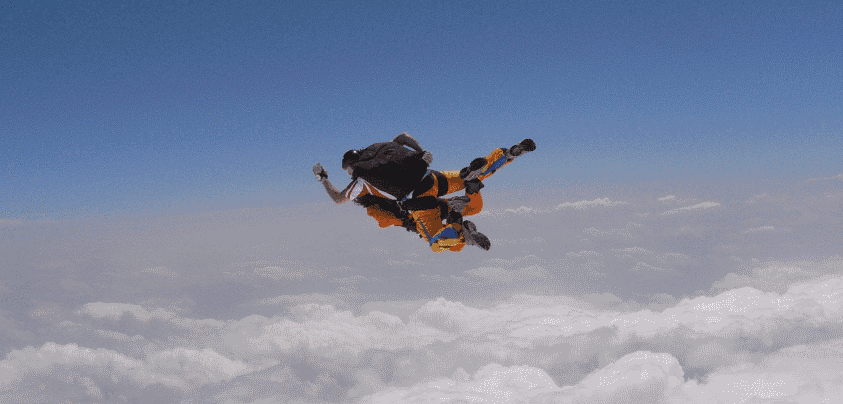 Skydiver in freefall above clouds Skydiver in freefall above a dense layer of clouds under clear blue sky.