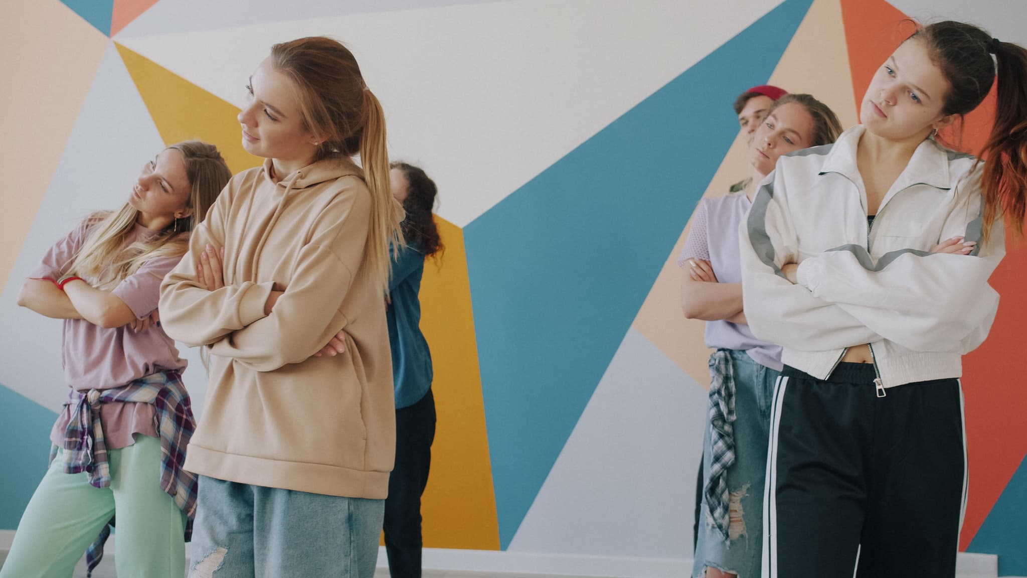 Diverse Group Against Geometric Wall Group of people standing together against a colorful geometric wall with blue, yellow, orange, and beige triangular shapes.