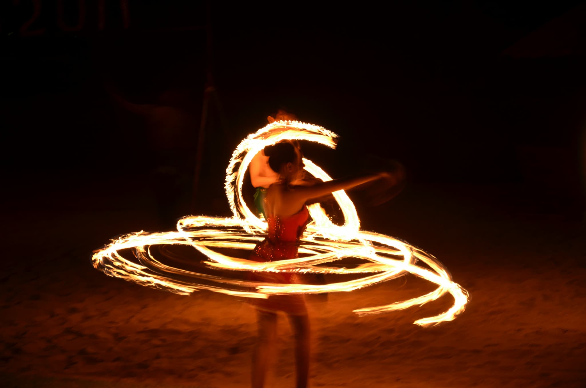 Feuerpoi-Performance Person führt nachts eine Feuerpoi-Performance auf und erzeugt mit brennenden Fackeln leuchtende Kreismuster.