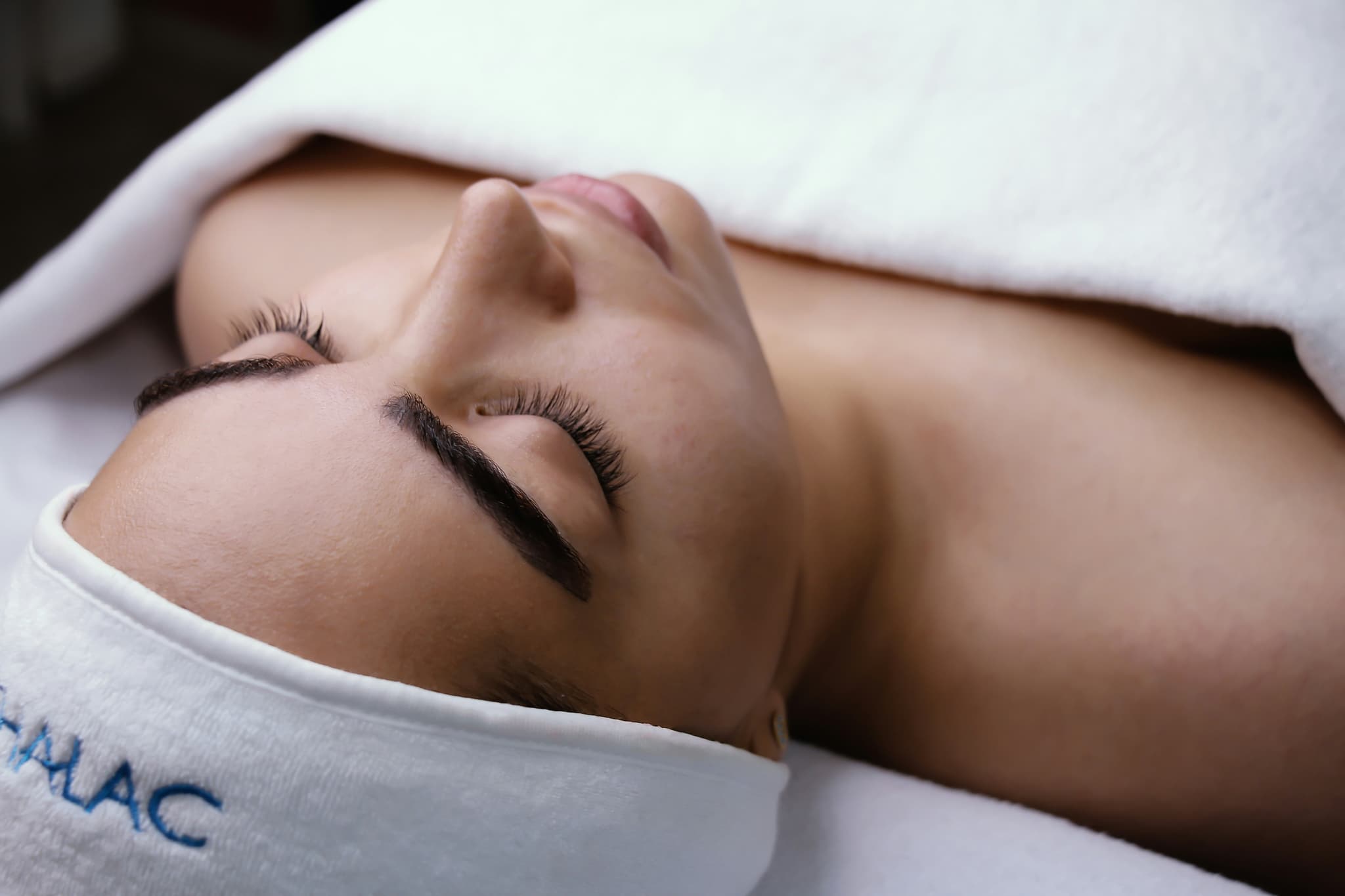 Spa Treatment and Relaxation Person lying down with eyes closed during a spa or wellness treatment, wrapped in white towels.