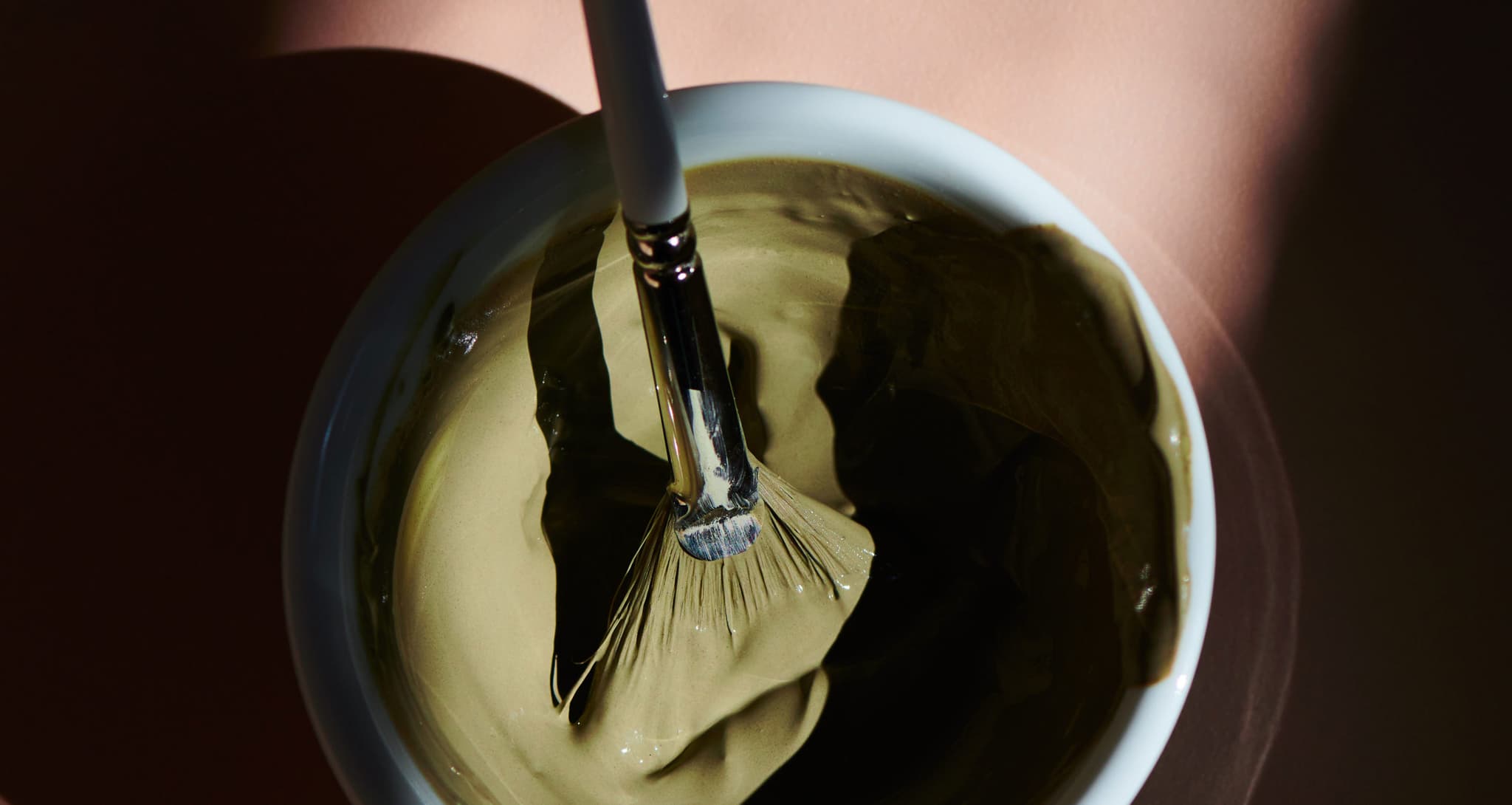 Pinsel in Gelbgrün getaucht Ein Pinsel, getaucht in einer weißen Schale mit gelbgrüner Farbe.