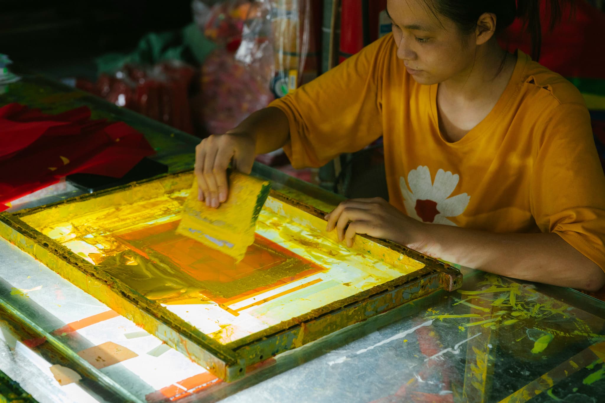 Silk Screen Printing Work in Progress Person in a yellow shirt working on a silk screen printing frame with yellow and orange ink.