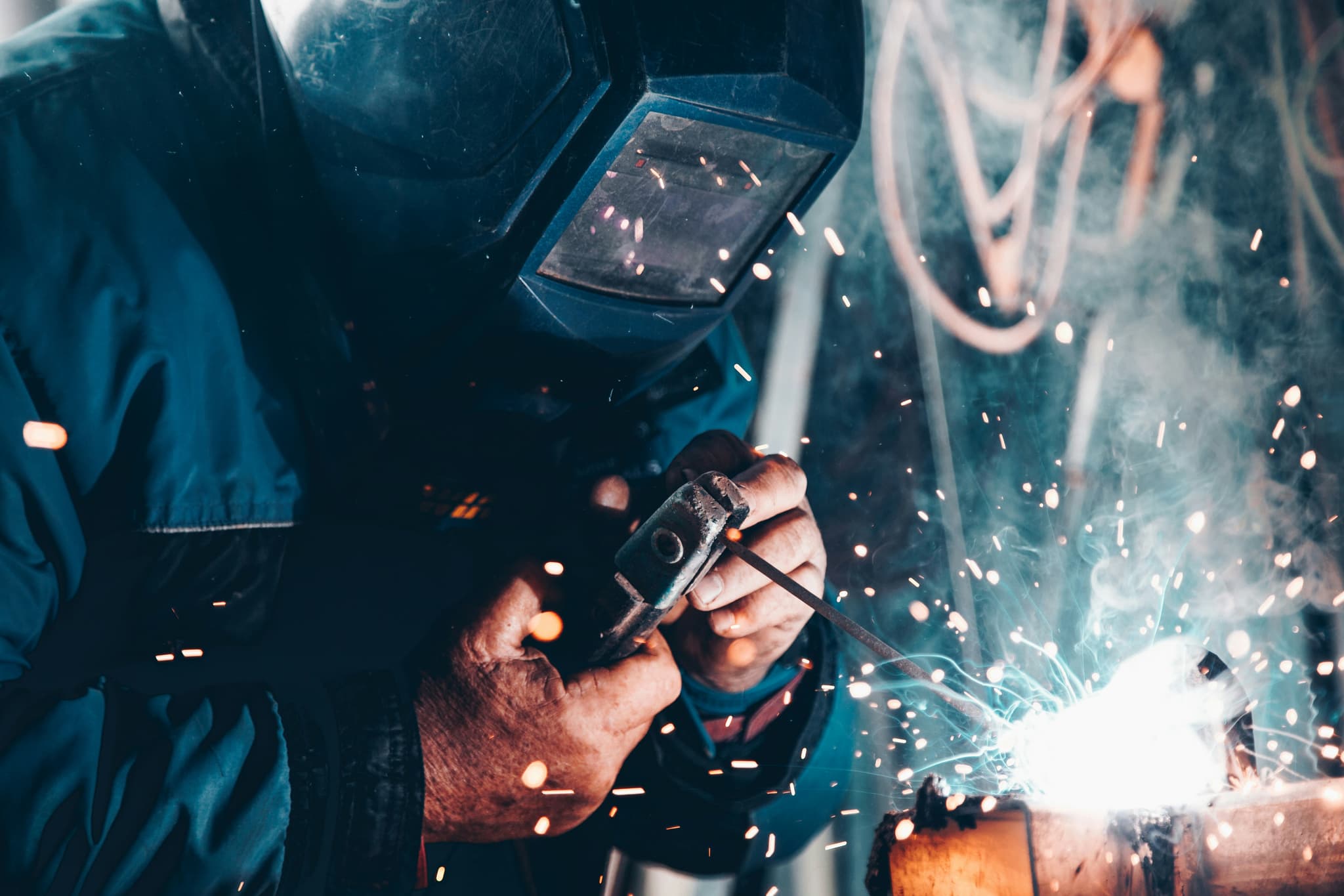 Welder With Protective Gear and Sparks Welder in protective gear and helmet working on metal with bright sparks flying.