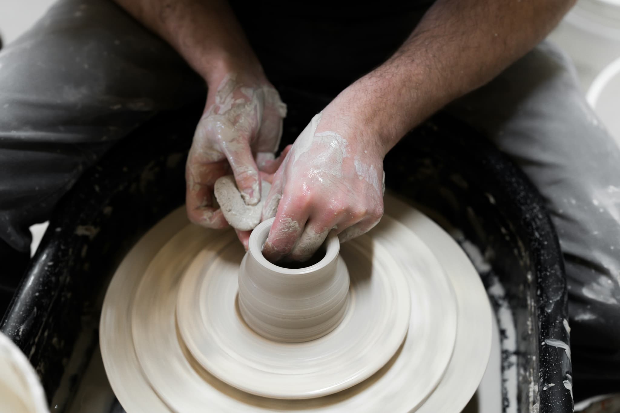 Hands Shaping Clay on Pottery Wheel Hands shaping wet clay on a pottery wheel during the centering stage.