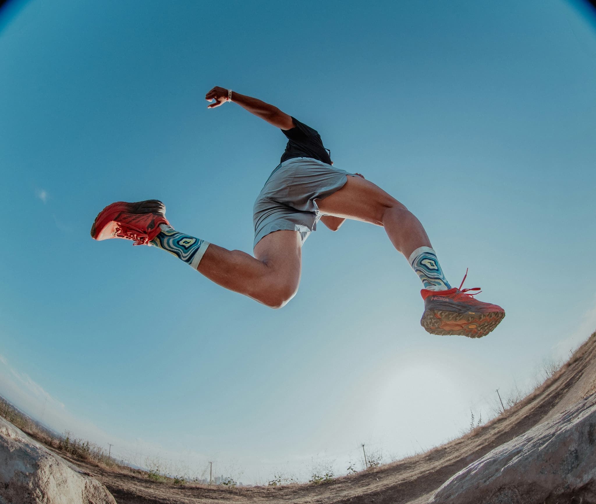 Runner Jumping Over Dirt Trail Runner in mid-air jumping over a dirt trail with clear blue sky in the background.