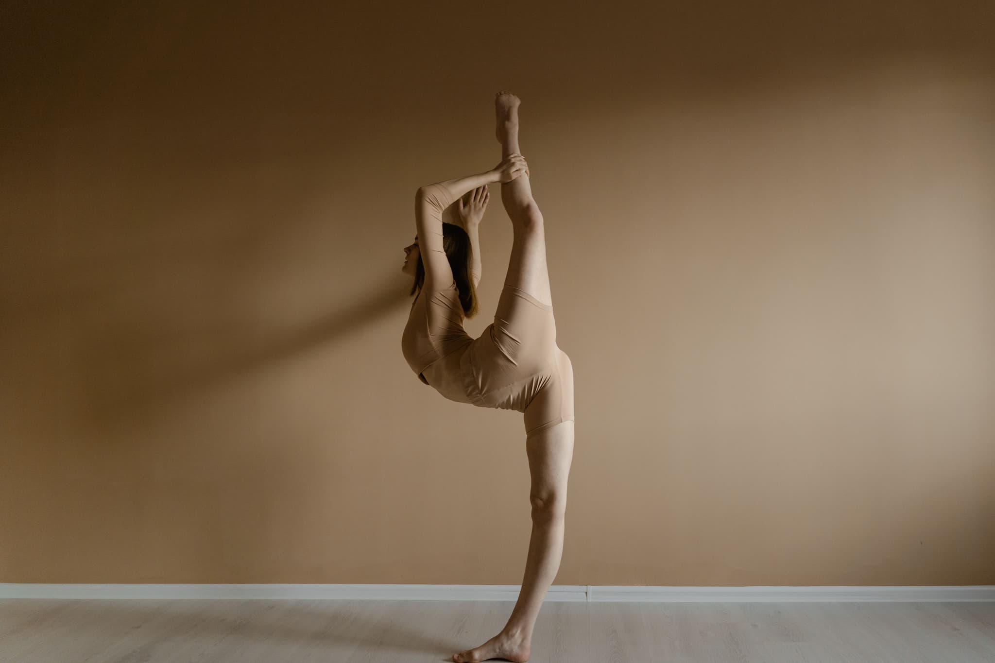 Dancer in Standing Split Pose Dancer performing a standing split pose in a neutral studio setting with a warm beige background.