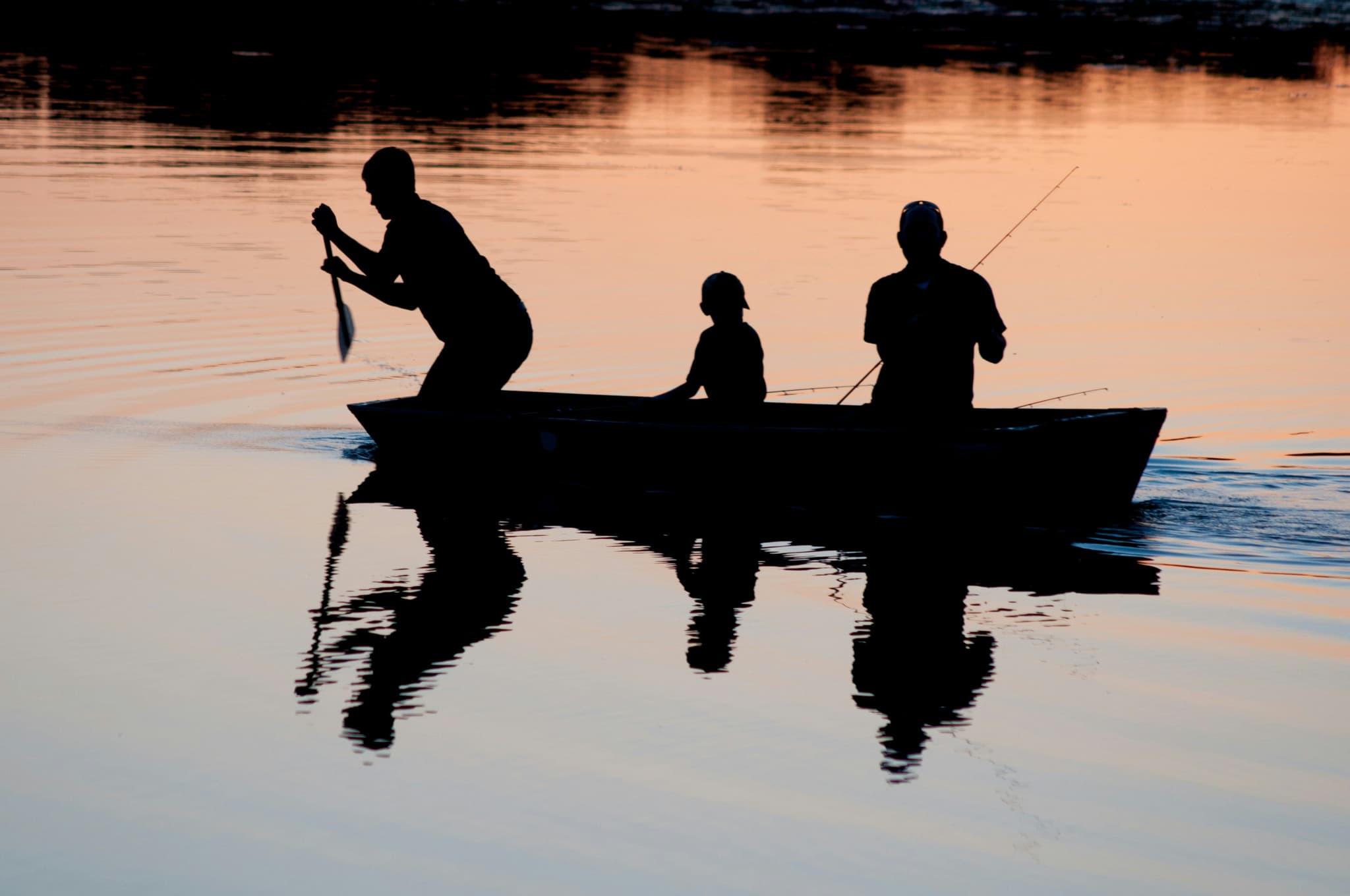 Fishing Boat at Sunset Three people fishing from a small boat on calm water at sunset, silhouetted against golden and blue tones