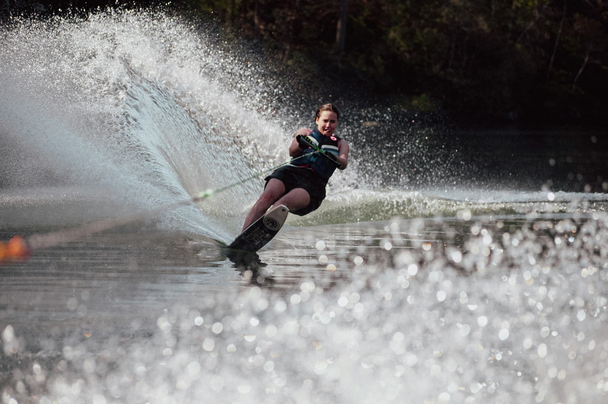 Wakeboarder Performing Water Trick Wakeboarder carving through water with a large spray behind them, towed by a rope.
