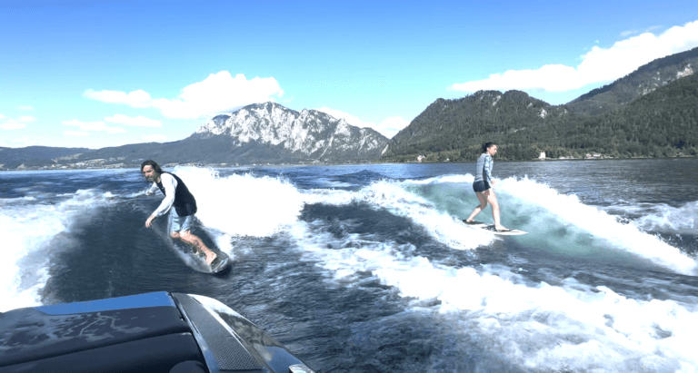 Wakeboarders on the Mountain Lake Two wakeboarders ride waves on a blue lake with snow-capped mountains in the background.