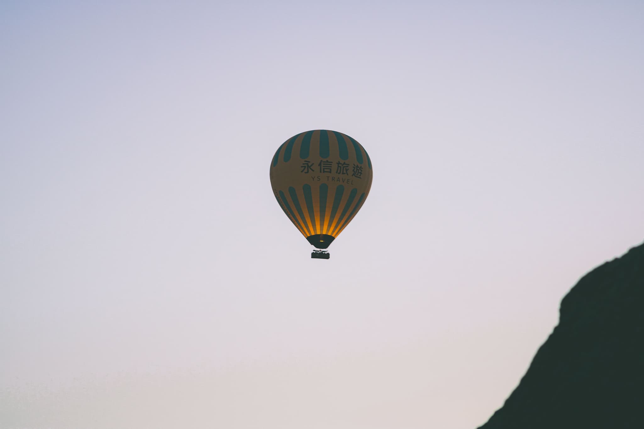 Hot Air Balloon in Flight Hot air balloon floating in a clear sky with striped envelope and mountain landscape below.