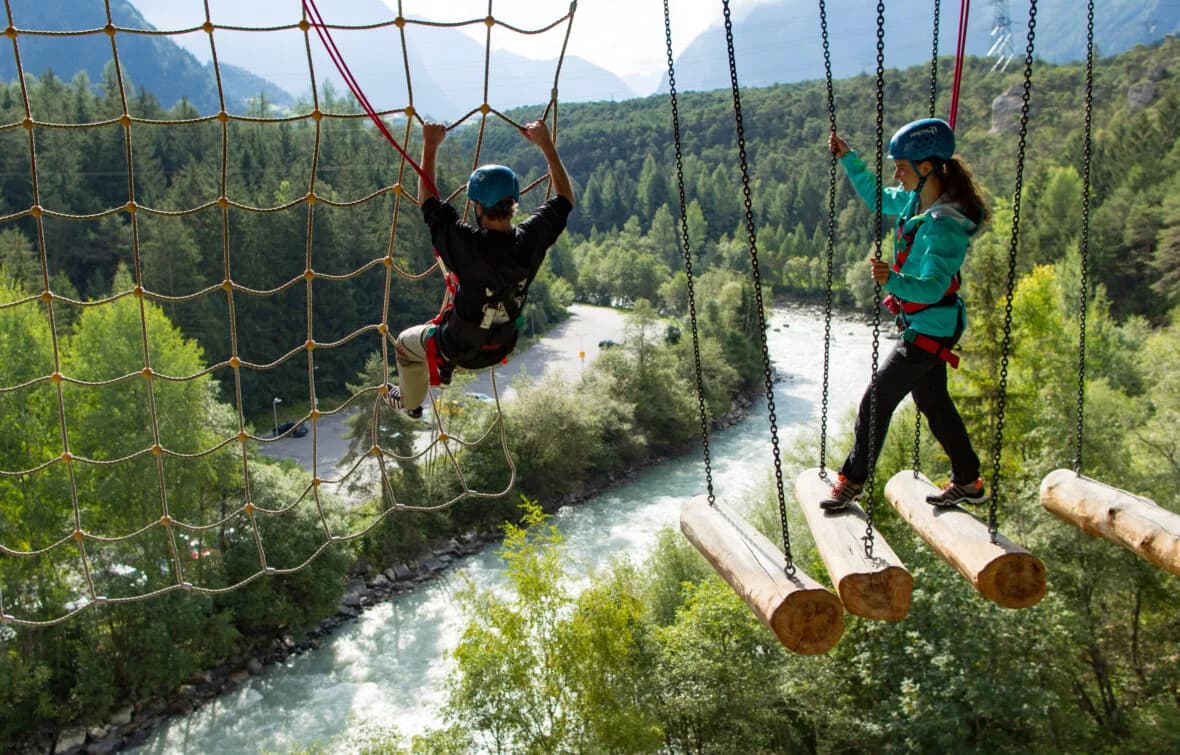High Ropes Course Over River Valley People crossing a high ropes course on hanging logs above a river valley.