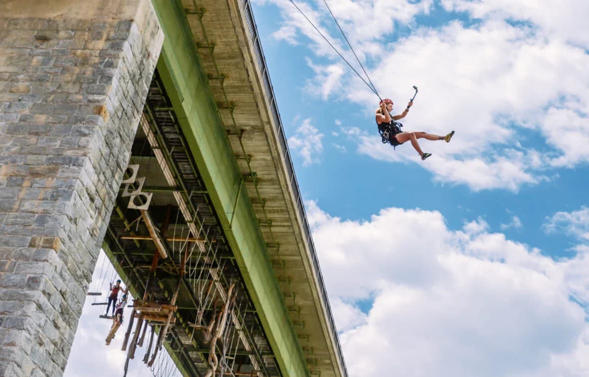 Bungee Jump From Bridge Into Sky Person bungee jumping off a bridge with clouds and blue sky behind them.