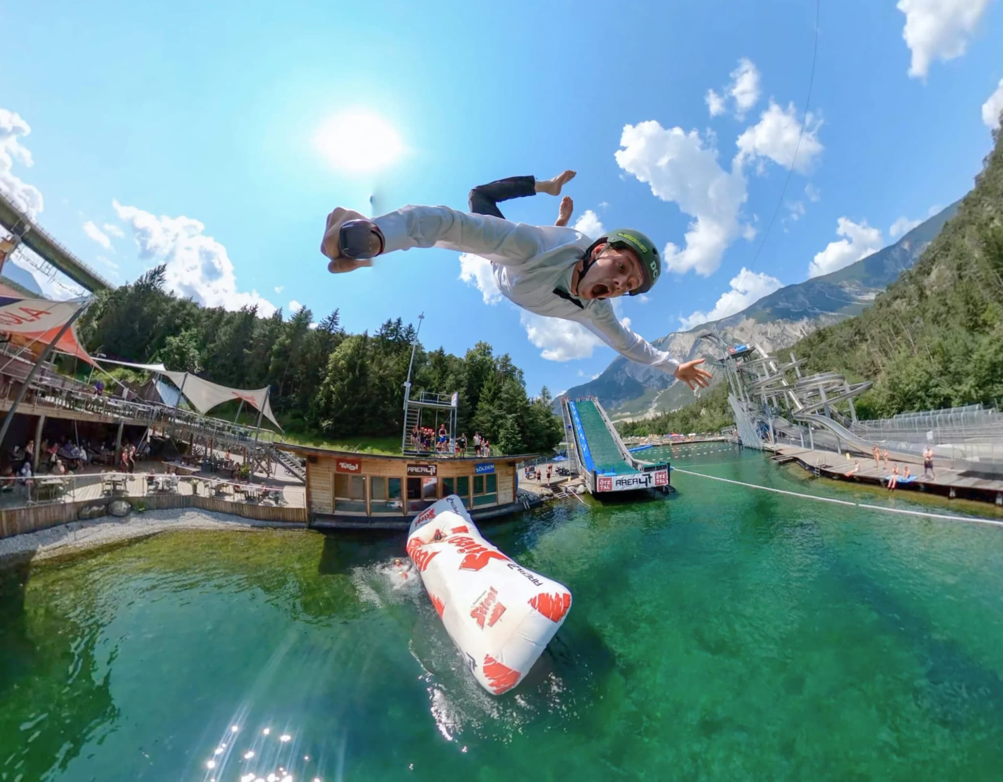 Airborne Jump Over Mountain Lake Person soaring off an inflatable jump into a green mountain lake.